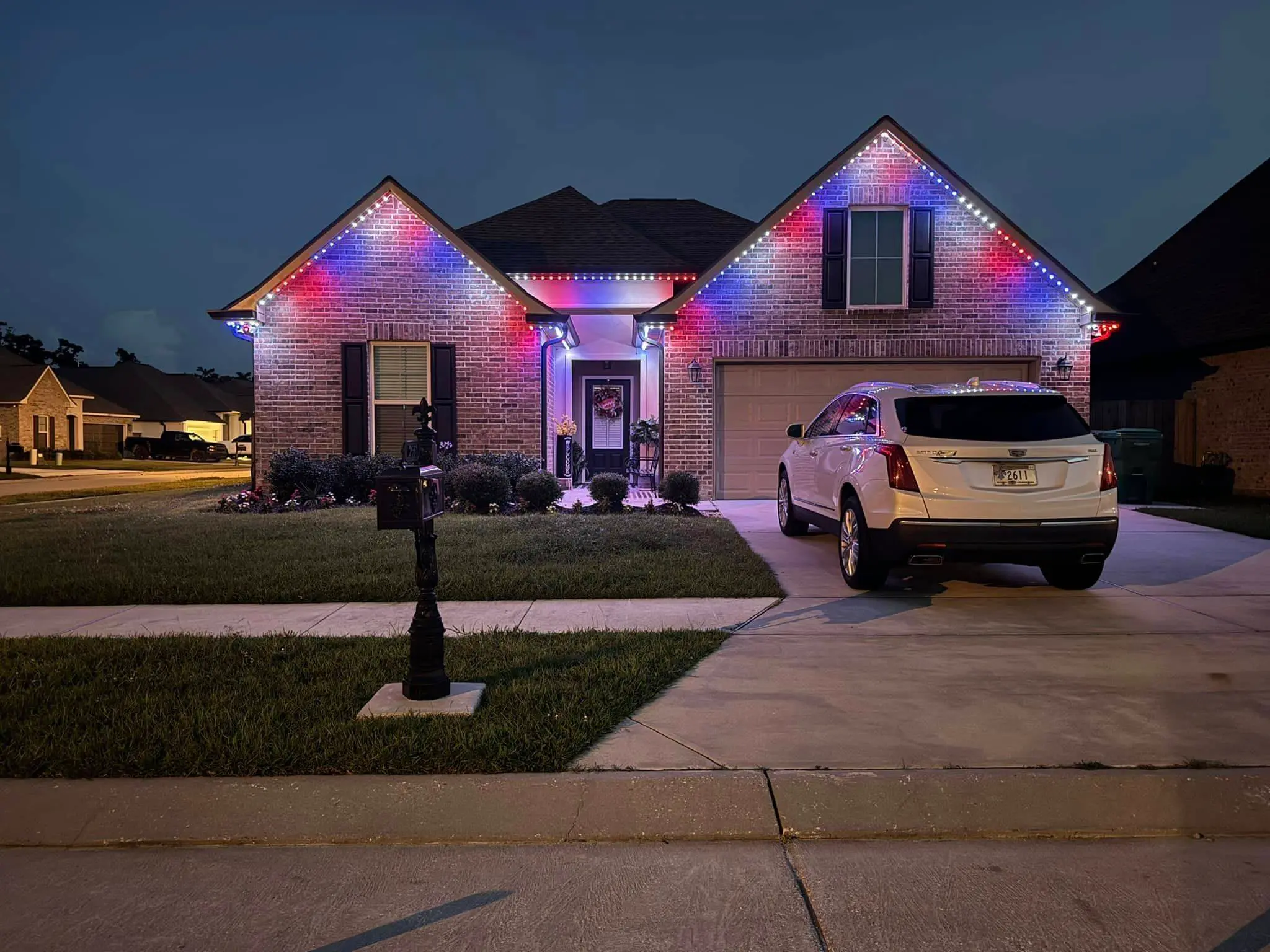 Brick house at night with red and blue Trimlight along both roof peaks.